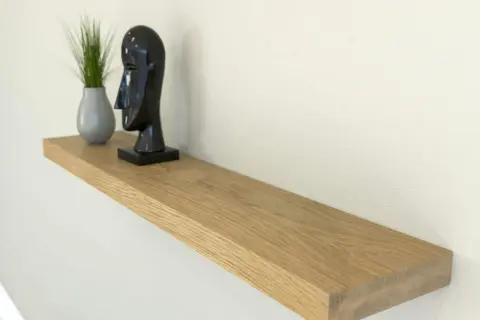 Estantería flotante de madera, ideal para poner baldas en pared sin escuadras. Decorada con un busto negro y una planta.