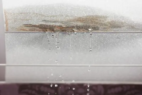 Gotas de agua caen de un techo manchado, señal de que la impermeabilización de tejados es urgente.