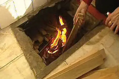 Manos añaden leña a un fuego en un hogar, brindando **gloria calefacción** a la estancia.
