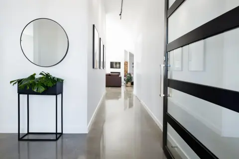 Pasillo moderno con suelo resina epoxi vivienda, espejo redondo, planta y puerta de cristal.