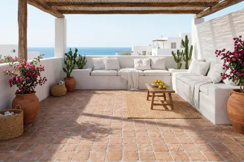 Terraza mediterránea con suelo de baldosas de terracota, sofás blancos, cactus y flores. Cumple la norma resbaladicidad c1, c2, c3.