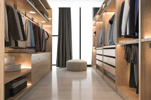 Un vestidor cerrado de madera clara, con ropa colgada y cajones organizados. Un puf beige y cortinas oscuras completan la escena.
