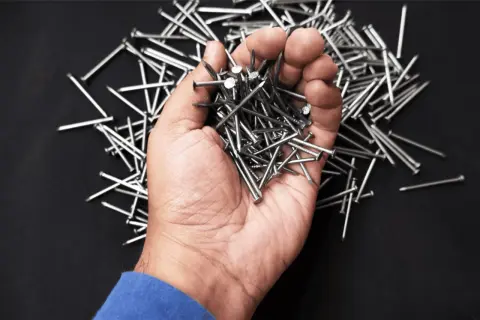 Una mano sostiene un montón de clavos, mostrando varios tipos de clavos sobre un fondo oscuro.