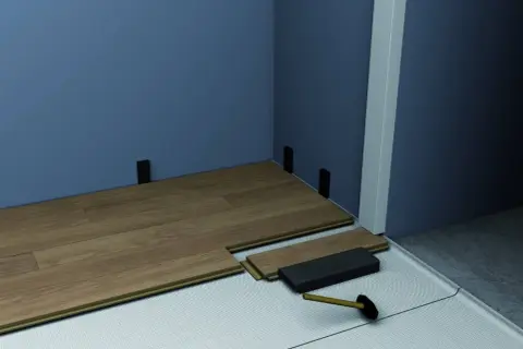 Instalación de suelo laminado con tacos para rodapiés. Se aprecian varios tipos de rodapiés y herramientas para su colocación.