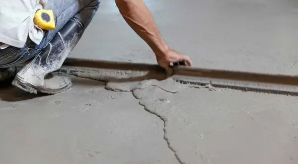 Obrero con botas y cinta métrica trabajando en como nivelar un suelo de cemento con una regla de albañil.