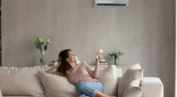 Mujer sonríe en el sofá, disfrutando de la temperatura ideal del aire acondicionado.