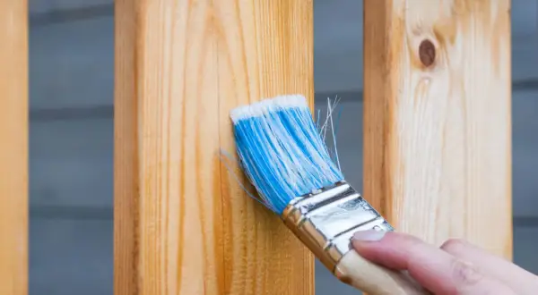 Pincel azul aplica protector a madera. Aprende como reparar madera dañada para restaurar su belleza y durabilidad.