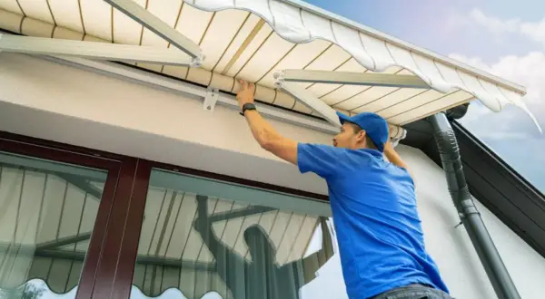 Hombre con gorra azul trabajando en la instalación o reparación de un toldo, ajustando la tela.