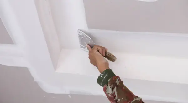 Mano con espátula aplica masilla para reparar techo escayola.