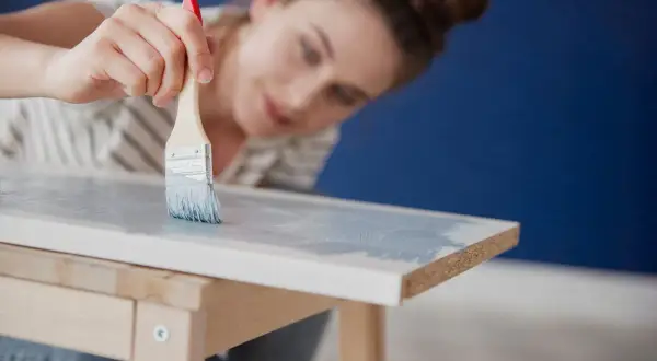 Mujer pintando muebles de melamina con brocha y pintura azul claro.