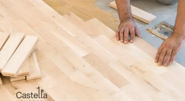 Man installing a light-colored suelo laminado, placing planks on adhesive.