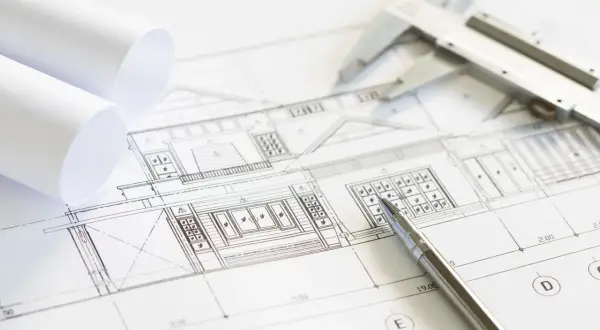 Plano arquitectónico con un **muro de carga** detallado. Se observan rollos de papel, un calibrador y un bolígrafo, listos para el diseño.