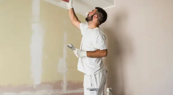 Hombre enmasillando techo y pared. Presupuesto para pintar piso.
