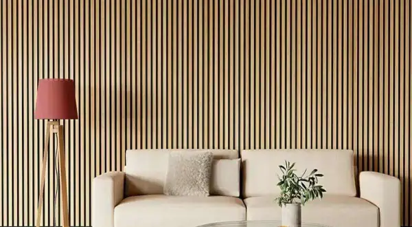 Una pared con listones de madera verticales, ideal para quienes buscan ideas sobre como poner listones de madera en la pared. Un sofá beige y una lámpara roja completan la escena.
