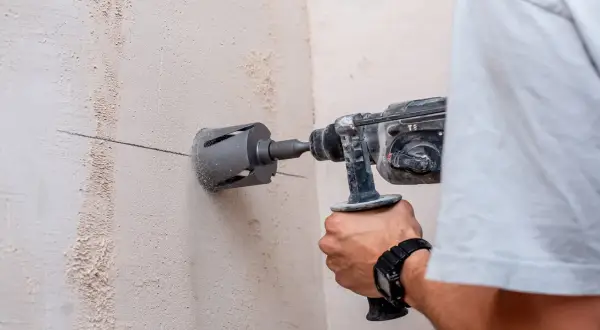 Un hombre usa un taladro con corona para hacer un agujero en una pared de hormigón. Se puede taladrar una viga de hormigón con esta herramienta.