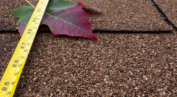 Medición de tejas en un metro cuadrado. Una hoja de otoño y cinta métrica sobre un tejado.