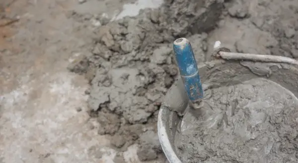 Paleta azul en un cubo con cemento fresco. El proceso de cómo hacer cemento es fundamental para la construcción.