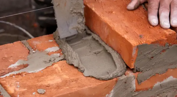 Mano coloca ladrillo sobre mortero fresco. Aprende como hacer mortero para construir.