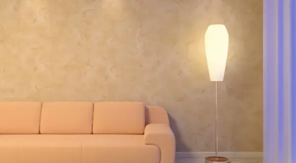 Sofá naranja junto a una lámpara de pie, con una pared texturizada que parece estucar una pared con un acabado rústico.