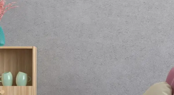 Estantería de madera con tazas, jarrón y un cojín sobre un sofá rosa. La pared tiene un acabado de gotelé, ideal para aplicar papel pintado sobre gotele.