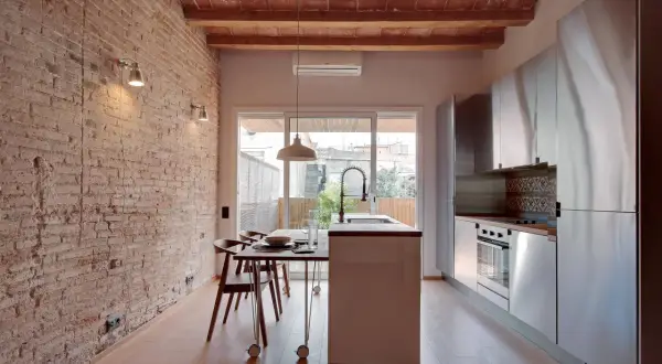 Cocina moderna con pared de ladrillo visto y pintura efecto envejecido. Vigas de madera en el techo y suelo de parqué.