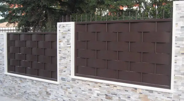 Muro de piedra con paneles de valla de metal marrón oscuro, un ejemplo de tipos de vallas para chalet.