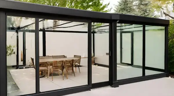 Modernos tipos de cerramientos de cristal con mesa y sillas en el interior, creando un espacio elegante y luminoso.
