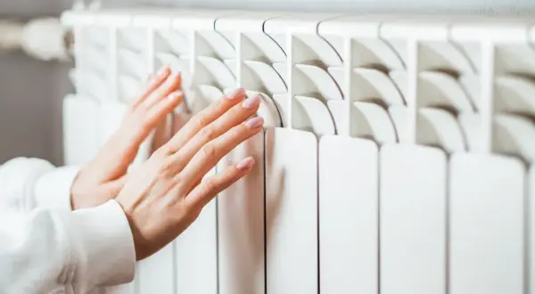 Manos tocando un radiador blanco. Aprende cómo limpiar radiadores para un hogar cálido y eficiente.
