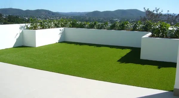 Terraza con césped artificial verde brillante y vistas a montañas. Podría haber inconvenientes de poner césped artificial en terraza, como el calor.