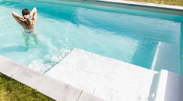 Mujer en bikini azul disfruta de su piscina cristalina, demostrando la facilidad de limpiar piscina sin vaciar agua.