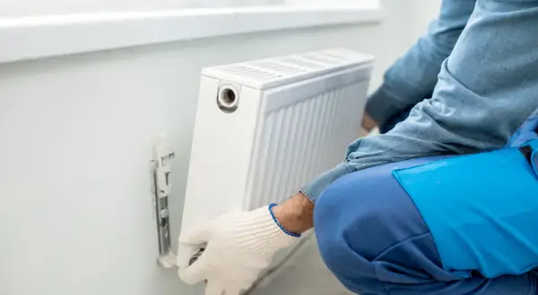 Man con guantes blancos ajusta un radiador blanco en la pared. Se está llevando a cabo la tarea de cambiar radiador de sitio.