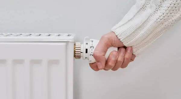 Mano ajustando el termostato de un radiador blanco. Parece que el radiador no calienta, a pesar de los ajustes.