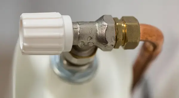 Detalle de una llave de radiador que gotea, con gotas de agua visibles en la conexión metálica.
