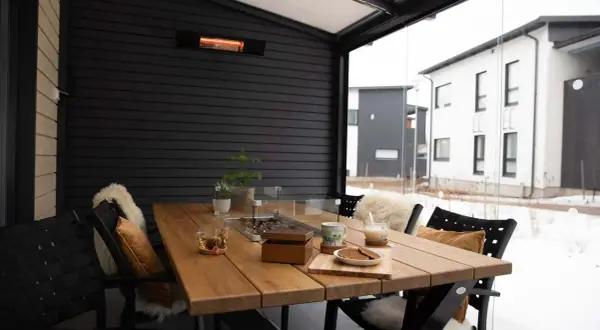 Mesa de madera en terraza cerrada con calefactor, ideal para disfrutar del exterior incluso con nieve.