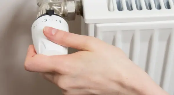 Mano ajustando el termostato de un radiador. Gira la perilla para abrir el radiador derecha o izquierda, regulando la temperatura.