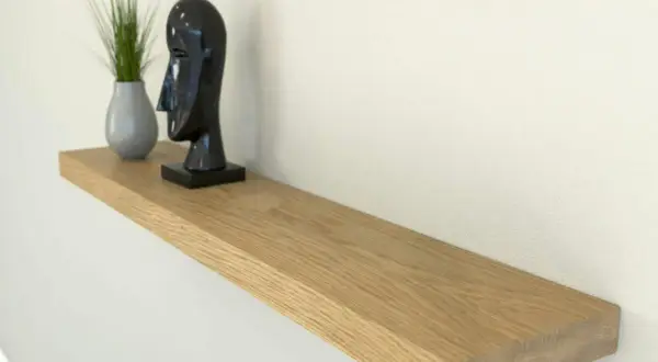 Estantería flotante de madera, ideal para poner baldas en pared sin escuadras. Decorada con un busto negro y una planta.