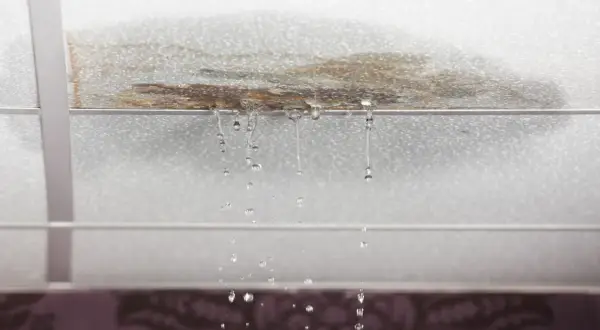 Gotas de agua caen de un techo manchado, señal de que la impermeabilización de tejados es urgente.