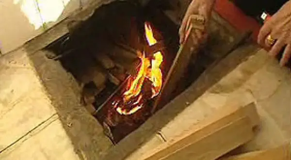 Manos añaden leña a un fuego en un hogar, brindando **gloria calefacción** a la estancia.