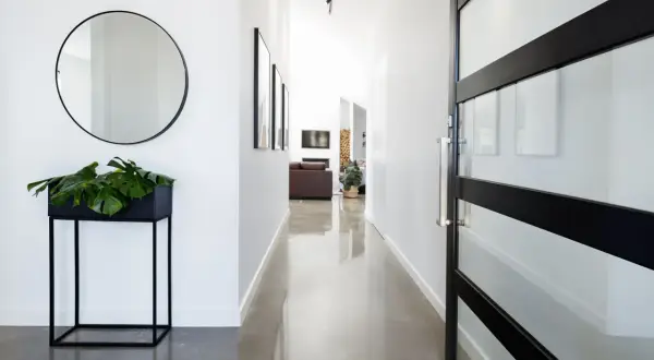 Pasillo moderno con suelo resina epoxi vivienda, espejo redondo, planta y puerta de cristal.