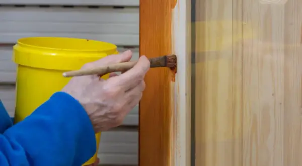 Persona aplica barniz a una puerta de madera con un pincel. El proceso de lacar puertas protege y embellece la madera.