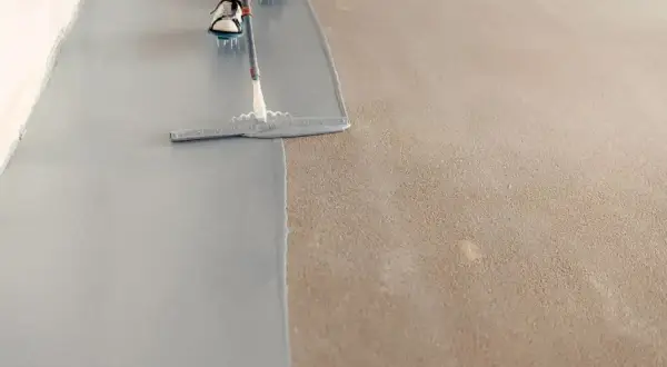 Persona pintando el suelo con una llana, aplicando una capa gris sobre una superficie texturizada.