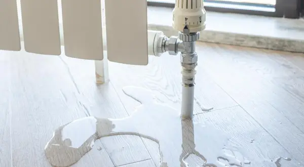 Fuga de agua en el suelo de madera cerca de un radiador. El agua se acumula, indicando la necesidad de quitar un radiador definitivamente.