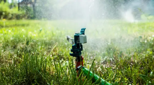 Aspersor de instalación de riego en acción, rociando agua sobre césped verde y frondoso bajo la luz del sol.