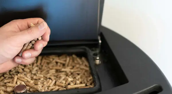 Mano añadiendo pellets a una estufa de leña. Preparando la instalación de estufa pellets para un invierno cálido.