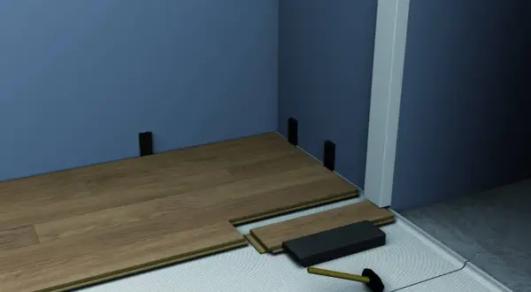 Instalación de suelo laminado con tacos para rodapiés. Se aprecian varios tipos de rodapiés y herramientas para su colocación.