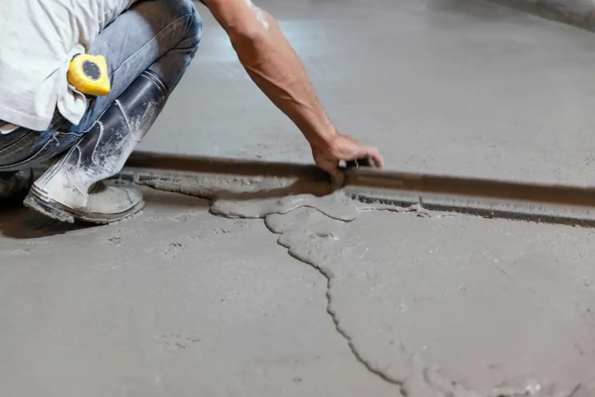 Obrero con botas y cinta métrica trabajando en como nivelar un suelo de cemento con una regla de albañil.