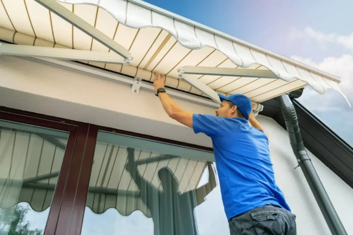 Hombre con gorra azul trabajando en la instalación o reparación de un toldo, ajustando la tela.