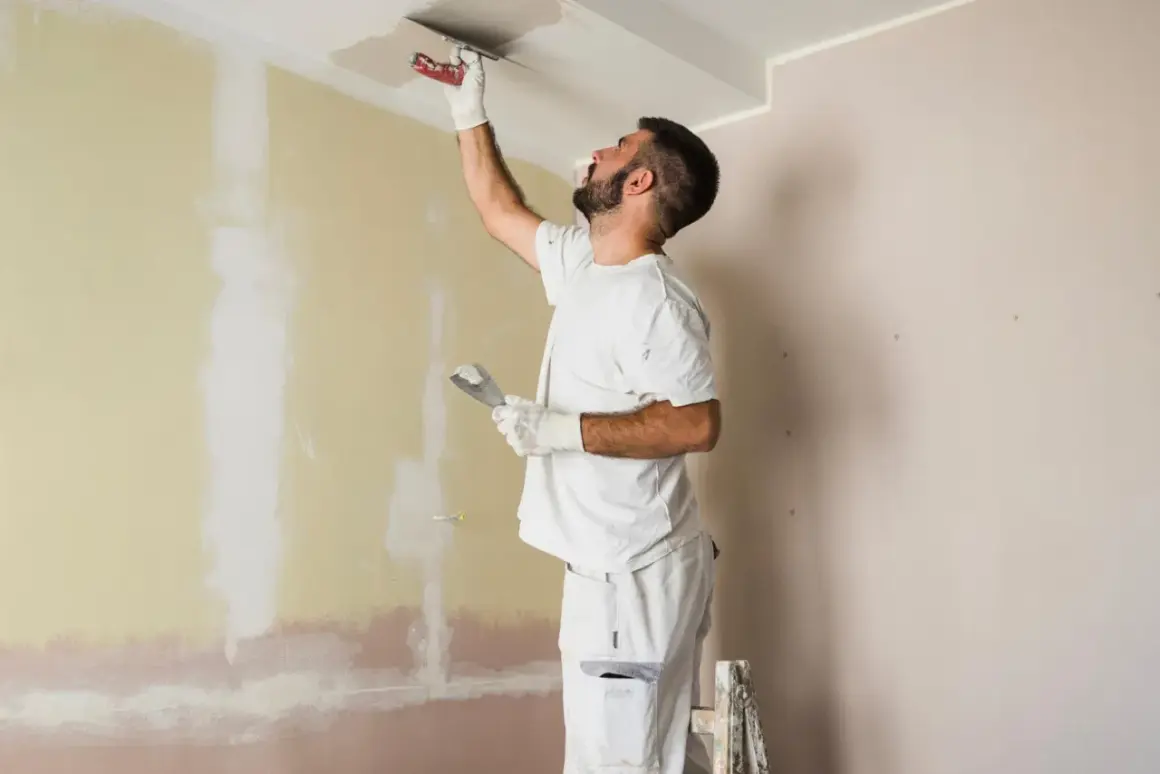 Hombre enmasillando techo y pared. Presupuesto para pintar piso.