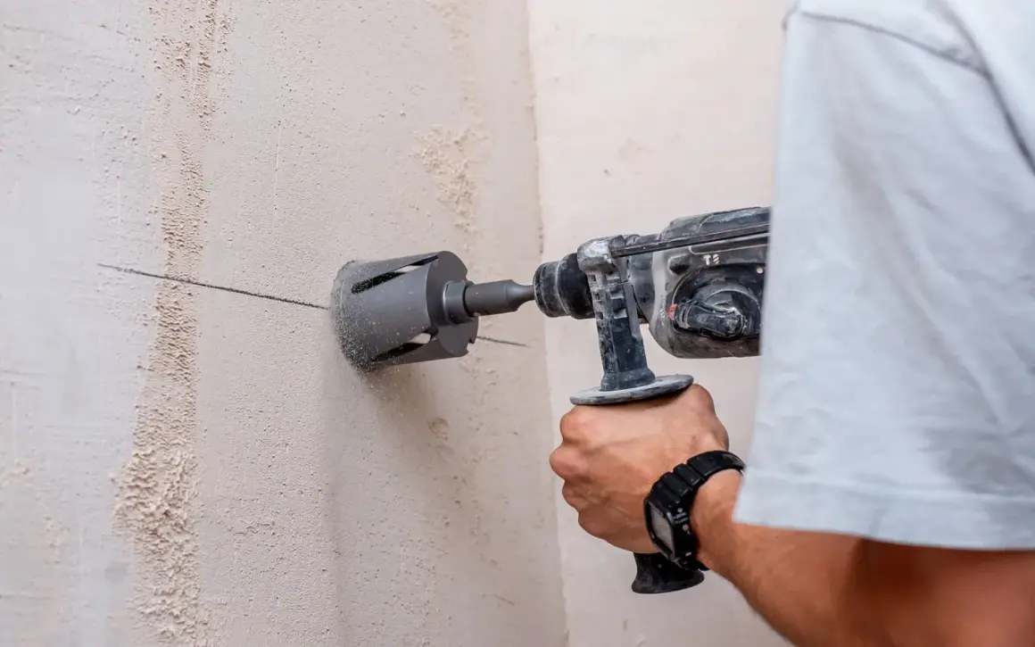 Un hombre usa un taladro con corona para hacer un agujero en una pared de hormigón. Se puede taladrar una viga de hormigón con esta herramienta.
