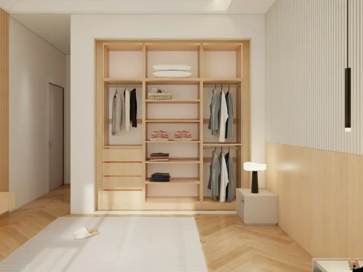 Armario empotrado de madera con puertas correderas, ropa colgada y doblada, y una lámpara de noche.